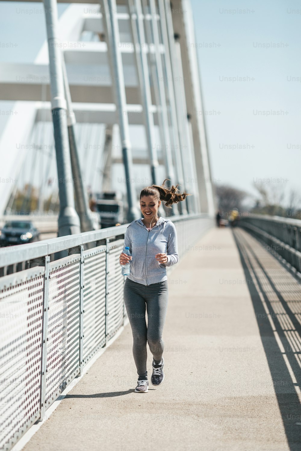 Schöne junge und fitte Frau in guter Form, die alleine auf der City Bridge Street läuft und joggt. Sie trägt sportliche Ohrhörer und hört Musik.