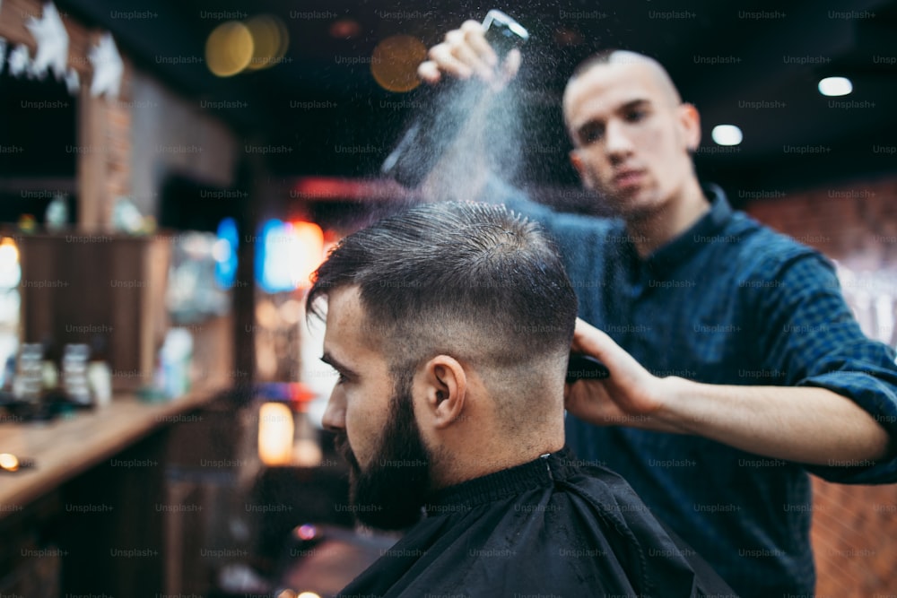 Homem jovem adulto de boa aparência recebendo um estilo de cabelo e barba e tratamento de curativo por cabeleireiro profissional.