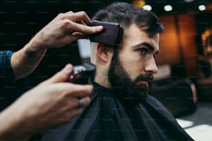 Giovane adulto di bell'aspetto che riceve un trattamento di acconciatura e vestizione di capelli e barba da parrucchiere professionista.