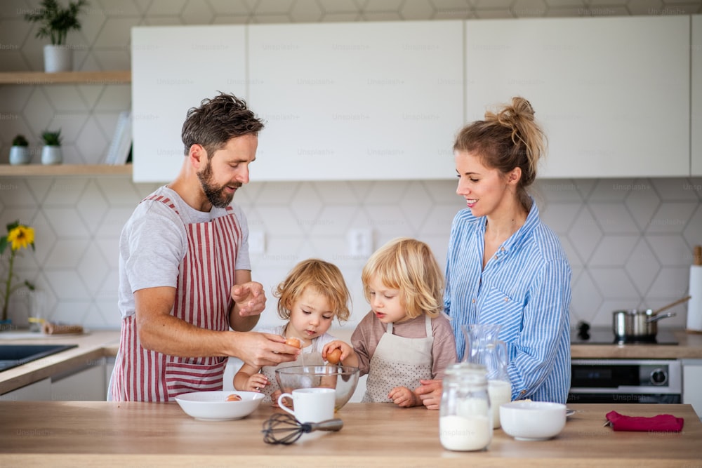 キッチンで2人の小さな子供を連れた若い家族の正面図、調理中に卵を割る。