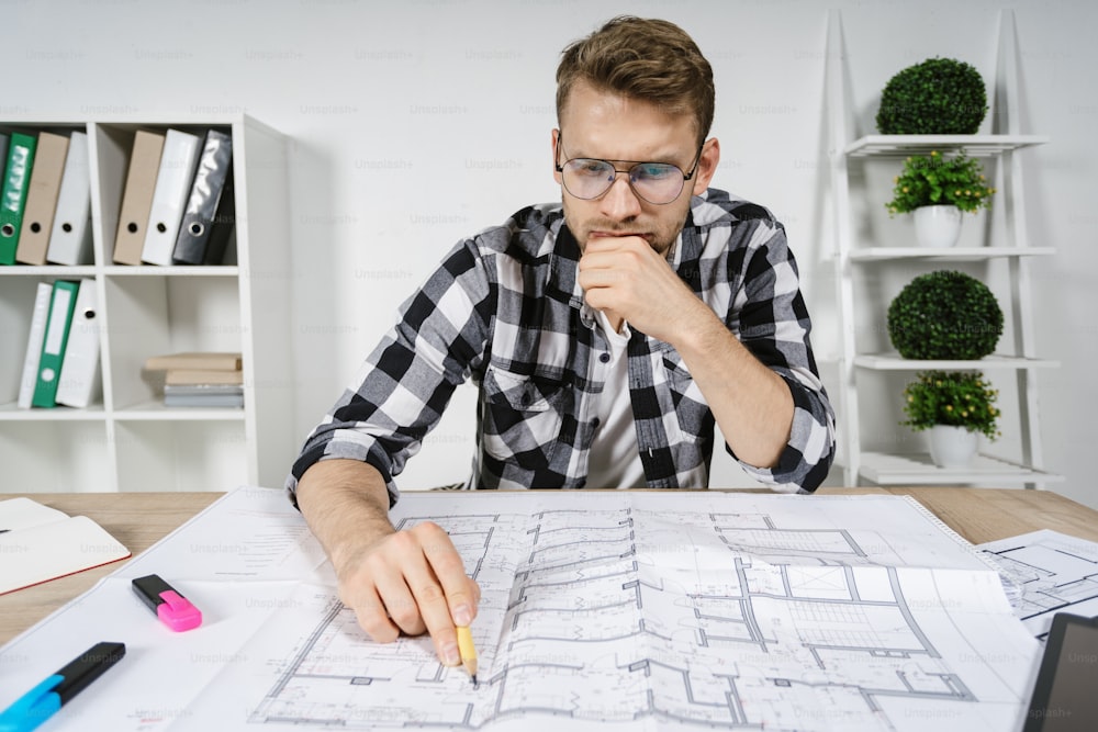 Minder and smart young adult architect working with blueprints in workspace office, checking solution for interior design in new house, making thoughtful face