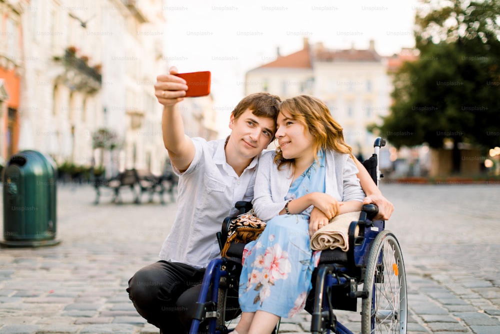 Happy couple in love taking selfie on the old city background - Disability concept with woman on wheelchair