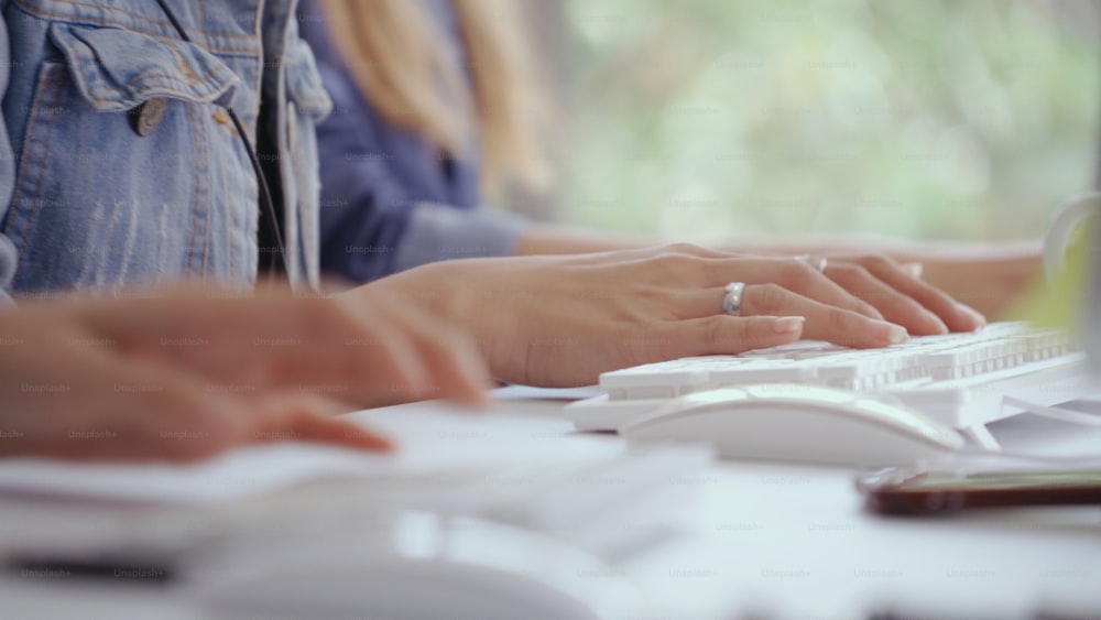 Primer plano de la mano de la mujer de negocios escribiendo a mano y trabajando en la computadora de escritorio en el escritorio de la oficina. Comunicación empresarial y concepto de lugar de trabajo.