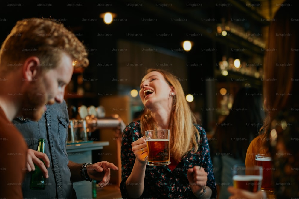Um pequeno grupo de melhores amigos em pé em um pub, bebendo cerveja, conversando e se divertindo. Concentre-se no barman limpando o copo. Vida noturna.