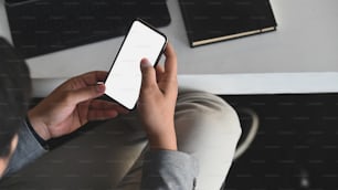 Close-up image of smart businessman is using a crop black smartphone with white blank screen on working desk.