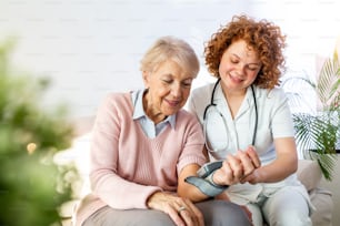 Cuidador midiendo la presión arterial de una mujer mayor en casa. Cuidador amable que mide la presión arterial de una anciana feliz en la cama de la residencia de ancianos.
