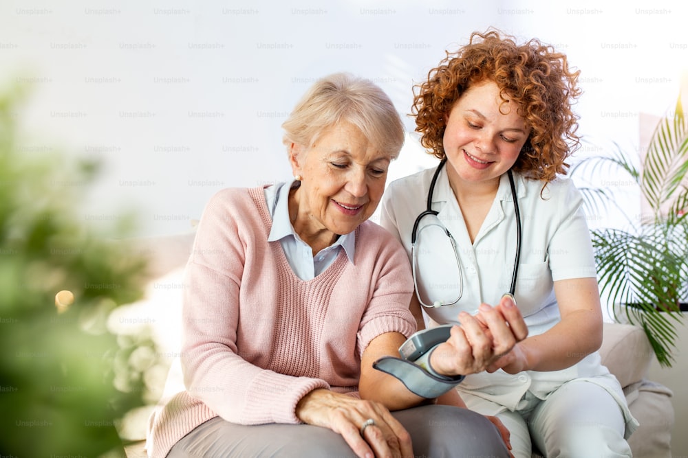 Caregiver che misura la pressione sanguigna di una donna anziana a casa. Gentile badante che misura la pressione sanguigna di una donna anziana felice a letto nella casa di cura.