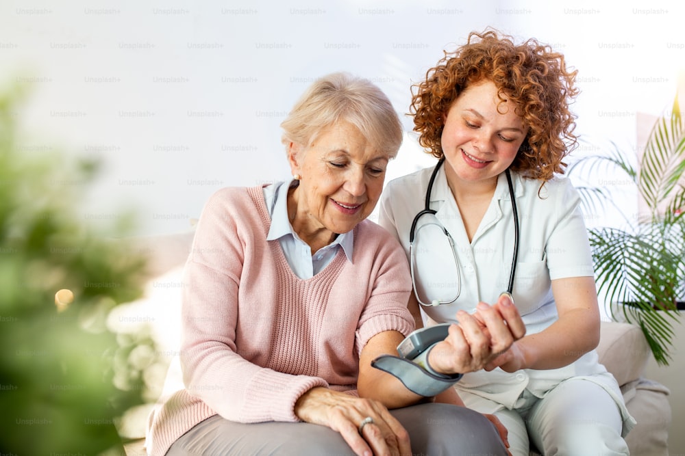 Caregiver measuring blood pressure of senior woman at home. Kind carer measuring the blood pressure of a happy elderly woman in bed in the nursing home.