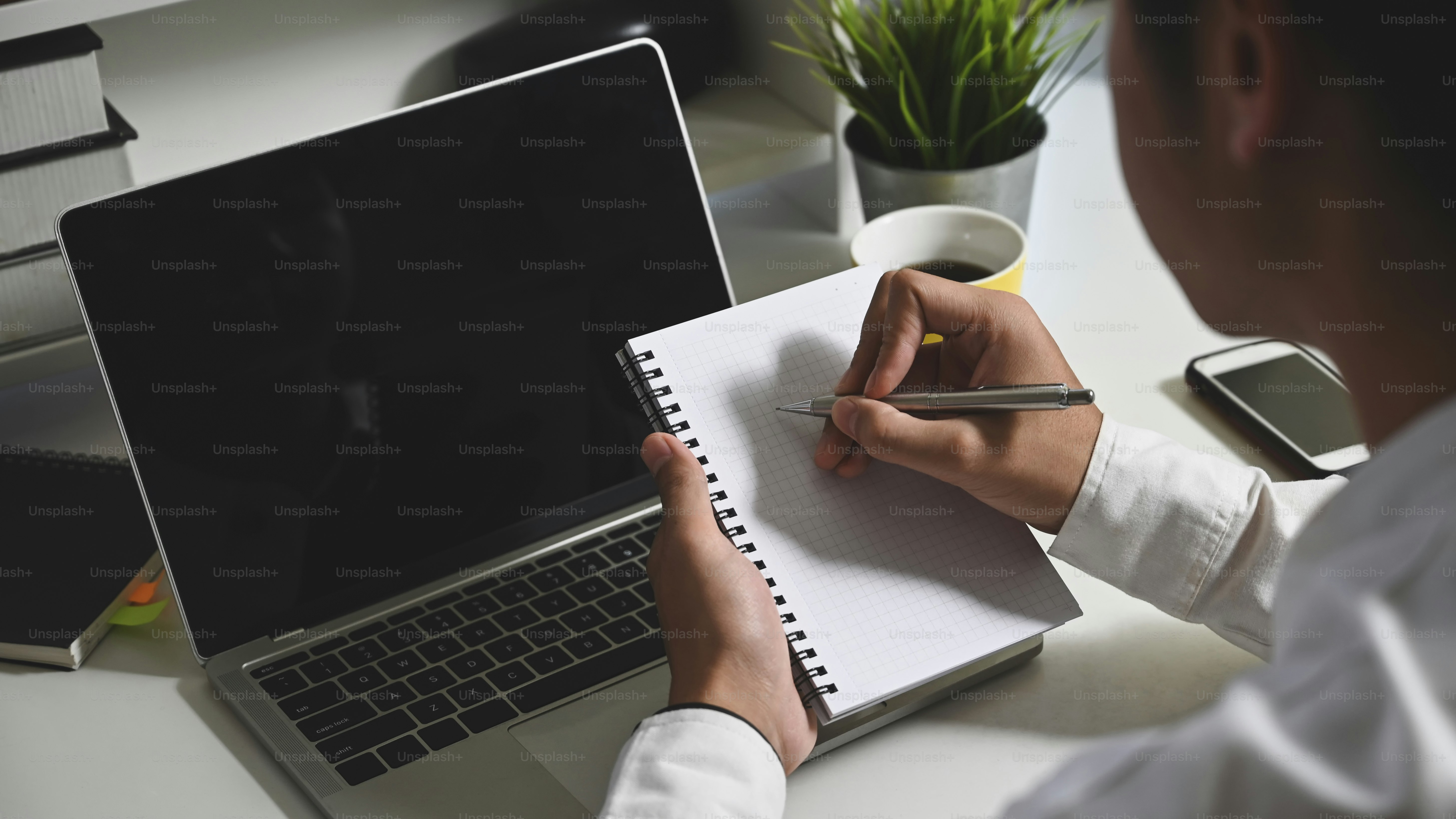Closeup business man taking notes in front black blank screen laptop at ...