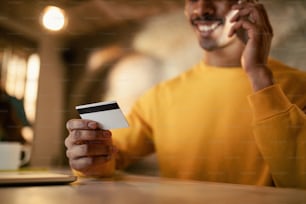 Close-up de empreendedor negro usando cartão de crédito ao fazer um telefonema à noite no escritório.