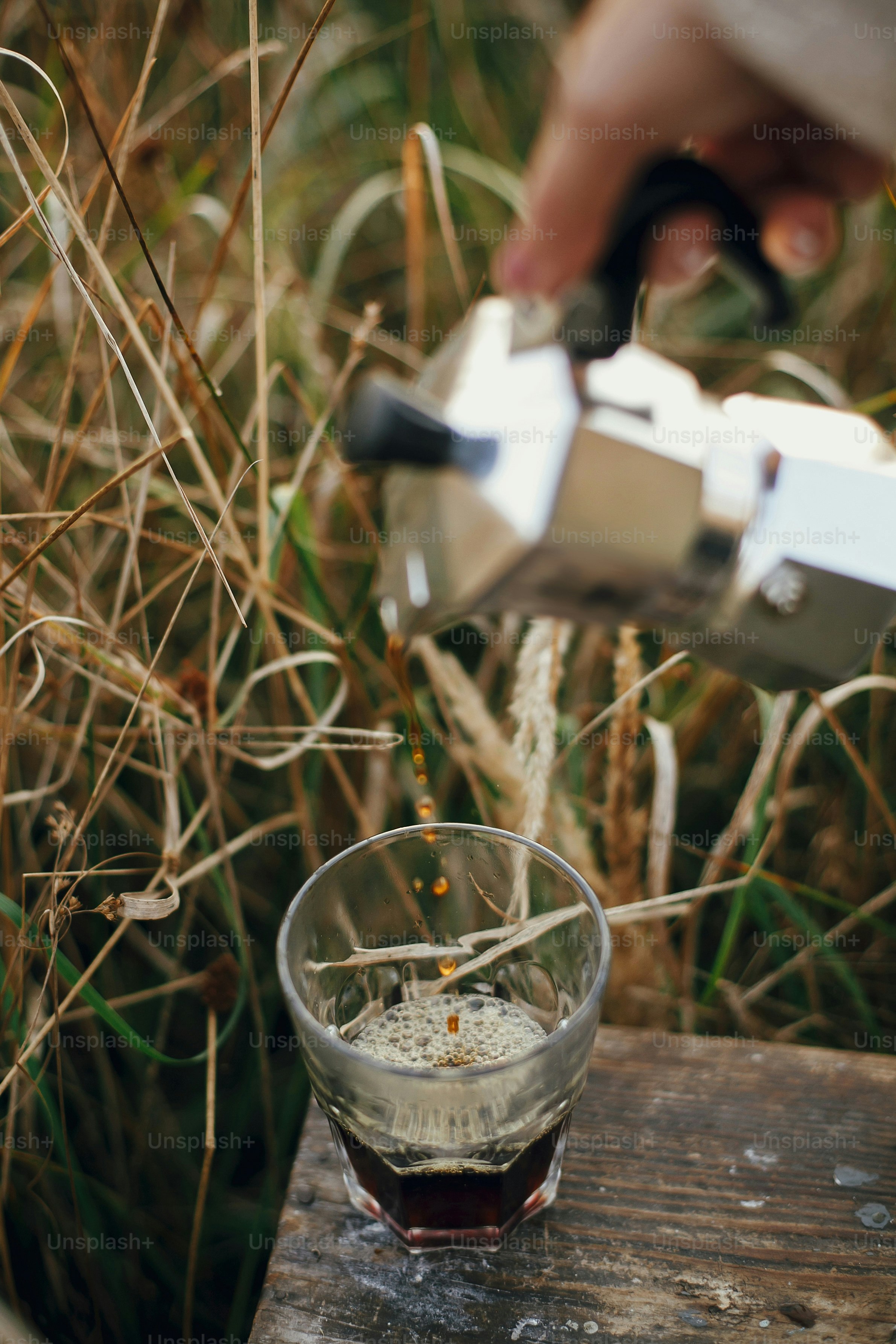 Alternative coffee brewing in travel. Pouring fresh hot coffee from geyser coffee maker into glass cup in sunny warm light in rural countryside herbs. Atmospheric moment. Vertical image