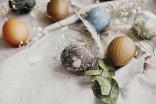Happy Easter. Stylish easter eggs on rustic table. Natural dyed colorful easter eggs with spring white flowers and feathers on rural textile background. Copy space