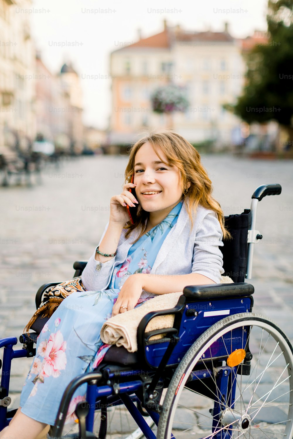 Giovane donna sorridente in sedia a rotelle che parla al telefono, lavora, consultazioni online, raccomandazioni online. Giovane donna d'affari in sedia a rotelle usando il telefono, all'aperto in città.