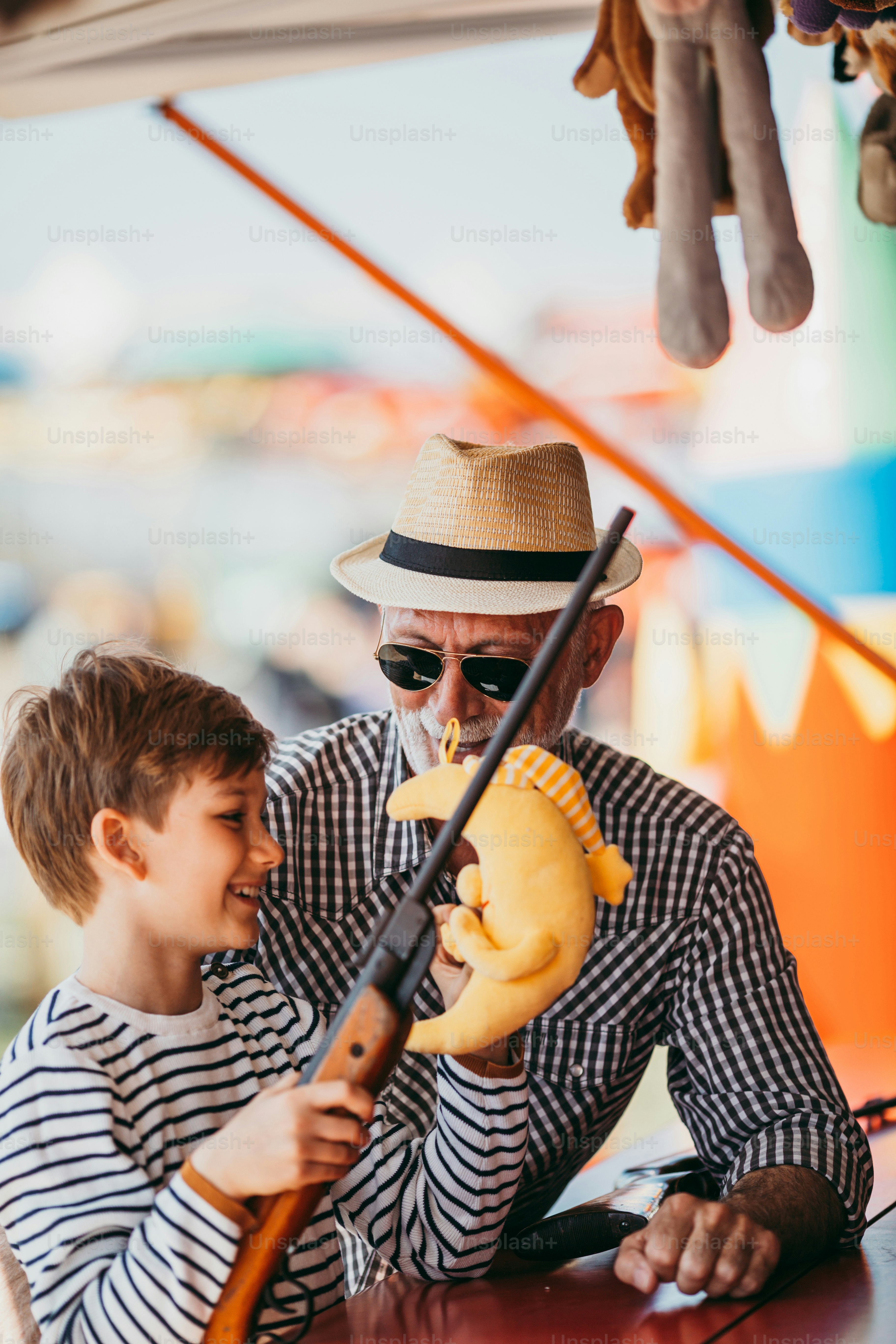 Nonno e nipote che si divertono e trascorrono del tempo di buona qualità insieme nel parco divertimenti. Bambino che spara con la pistola ad aria compressa mentre il nonno lo aiuta a vincere il premio.