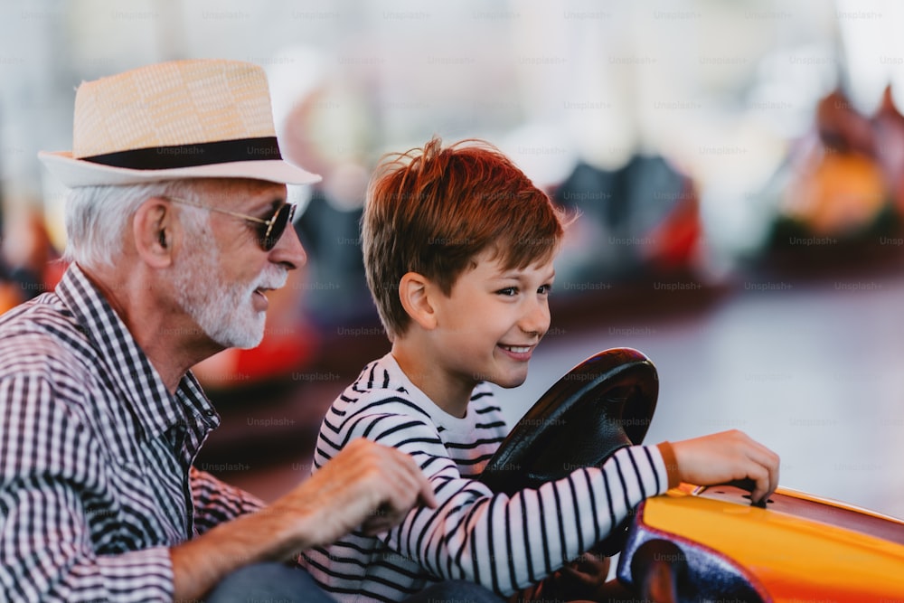 Nonno e nipote che si divertono e trascorrono del tempo di buona qualità insieme nel parco divertimenti. Si divertono e sorridono mentre guidano insieme l'autoscontro.