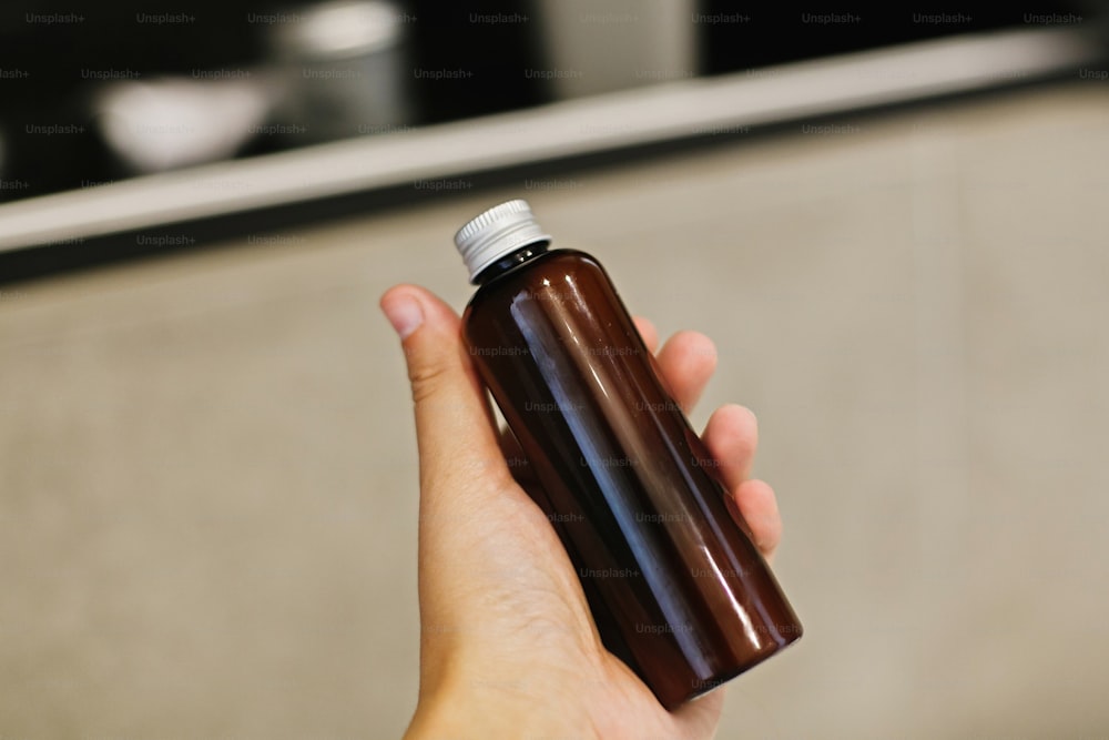 Hand holding natural tonic or shampoo in glass bottle in modern bathroom on background of stylish black shelf with plastic free natural organic essentials. Zero waste concept.