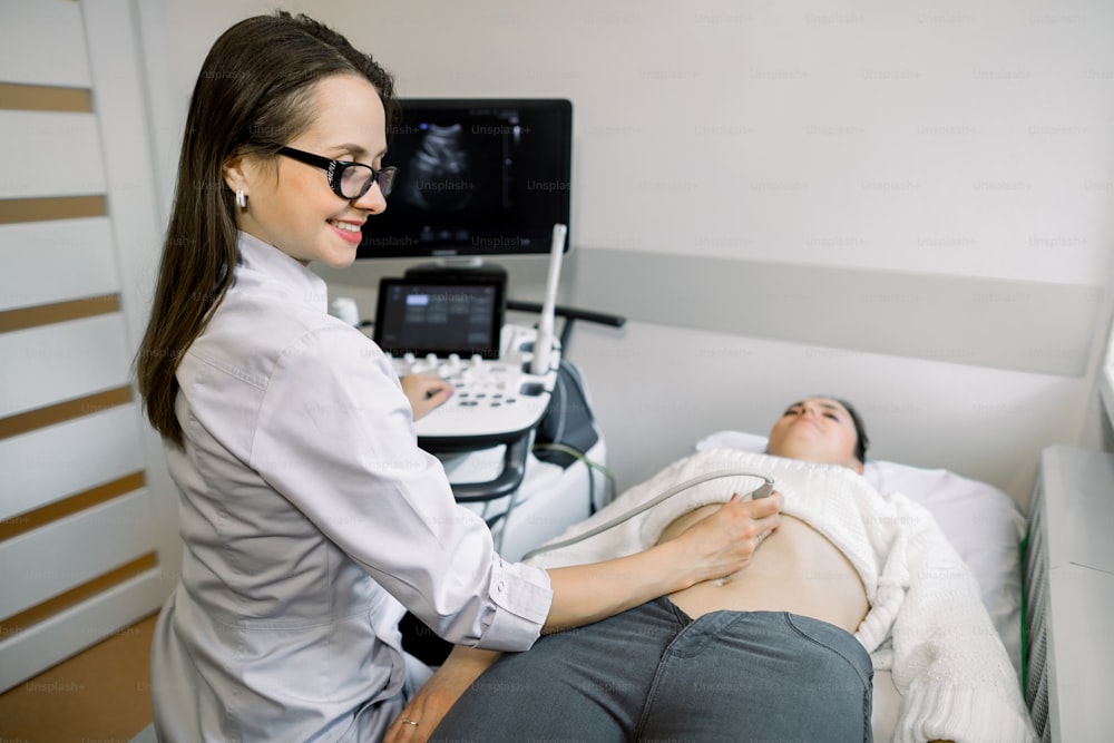 Ultrasound diagnostics of a young woman by modern ultrasound equipment. Pregnant woman getting ultrasound from female doctor.