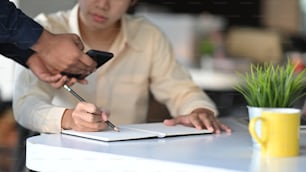 Cropped shot of young architect writing/drawing roughly the house architectural concept by copying from the customer smartphone.