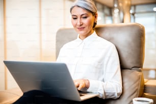 Mirthful adult lady sitting with a laptop on her knees and smiling while using it
