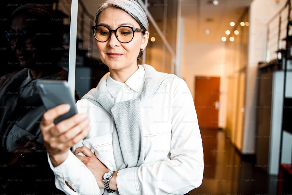 Smiling attractive business woman standing and looking at her smartphone