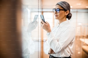 Calm attractive woman in a white shirt looking at the screen of her smartphone