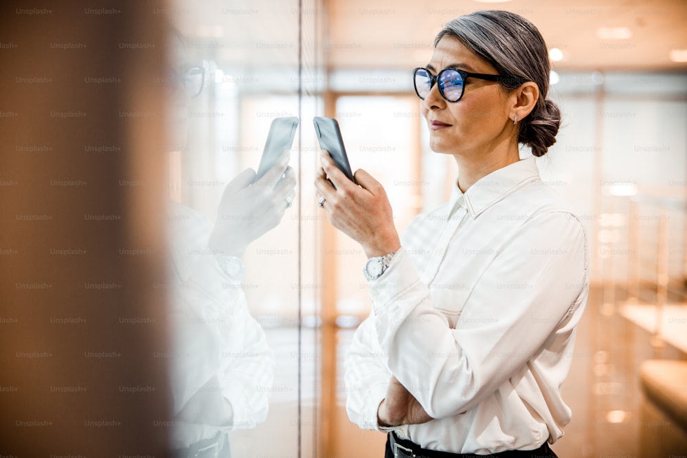 Calm attractive woman in a white shirt looking at the screen of her smartphone