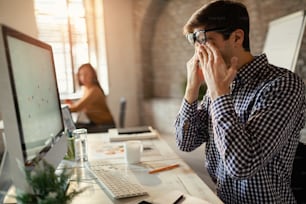 Empresario masculino que se siente agotado mientras analiza gráficos de negocios en una PC de escritorio en la oficina.