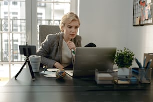 Waist up of young female blogger sitting at desktop while working with laptop
