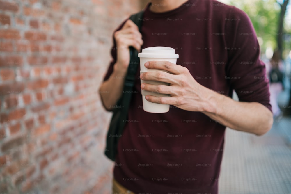 路上で屋外でコーヒーを飲みながら歩いている若い男性の肖像画。アーバンコンセプト。