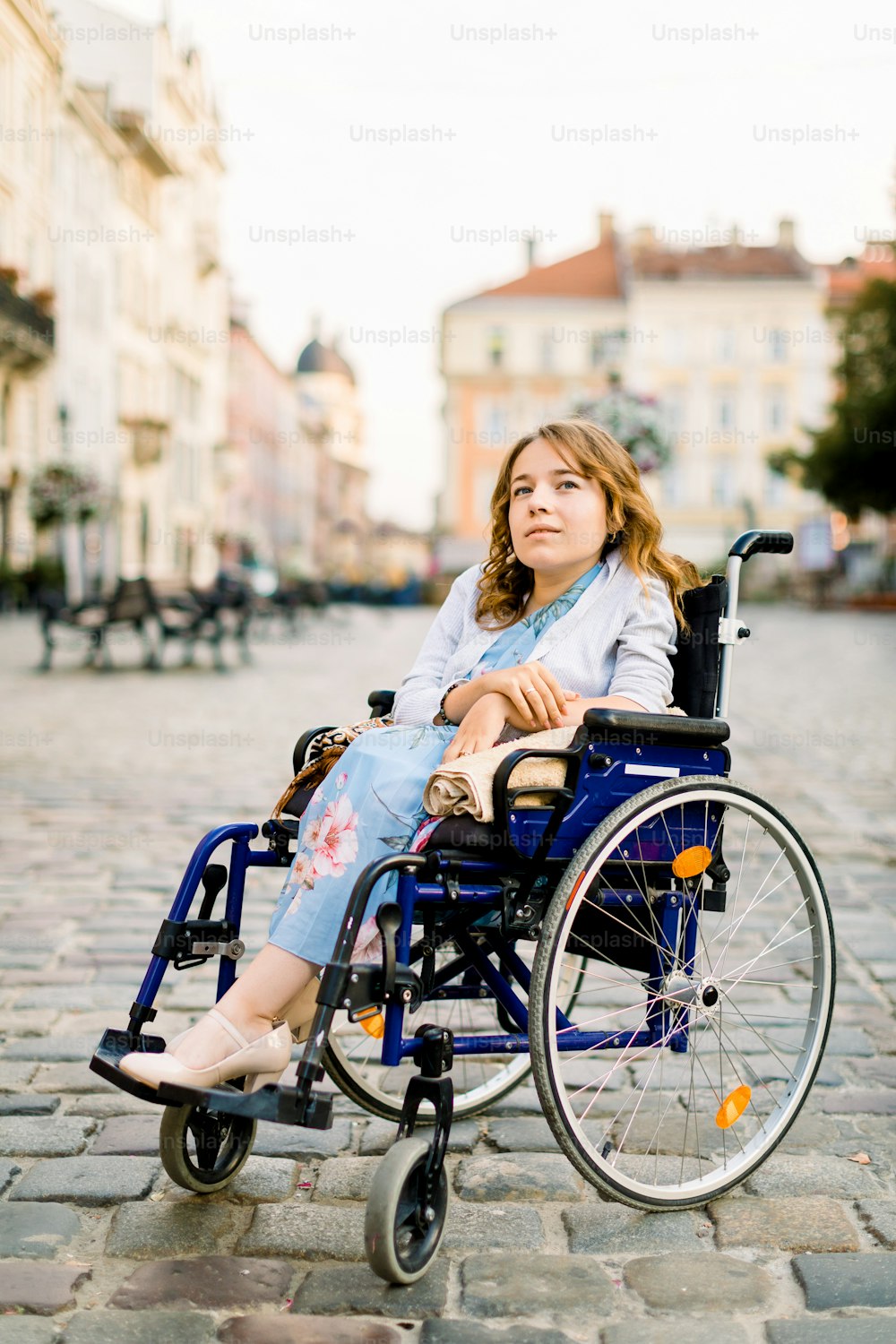 Mulher jovem feliz na cadeira de rodas ao ar livre, posando no fundo de edifícios antigos na cidade.