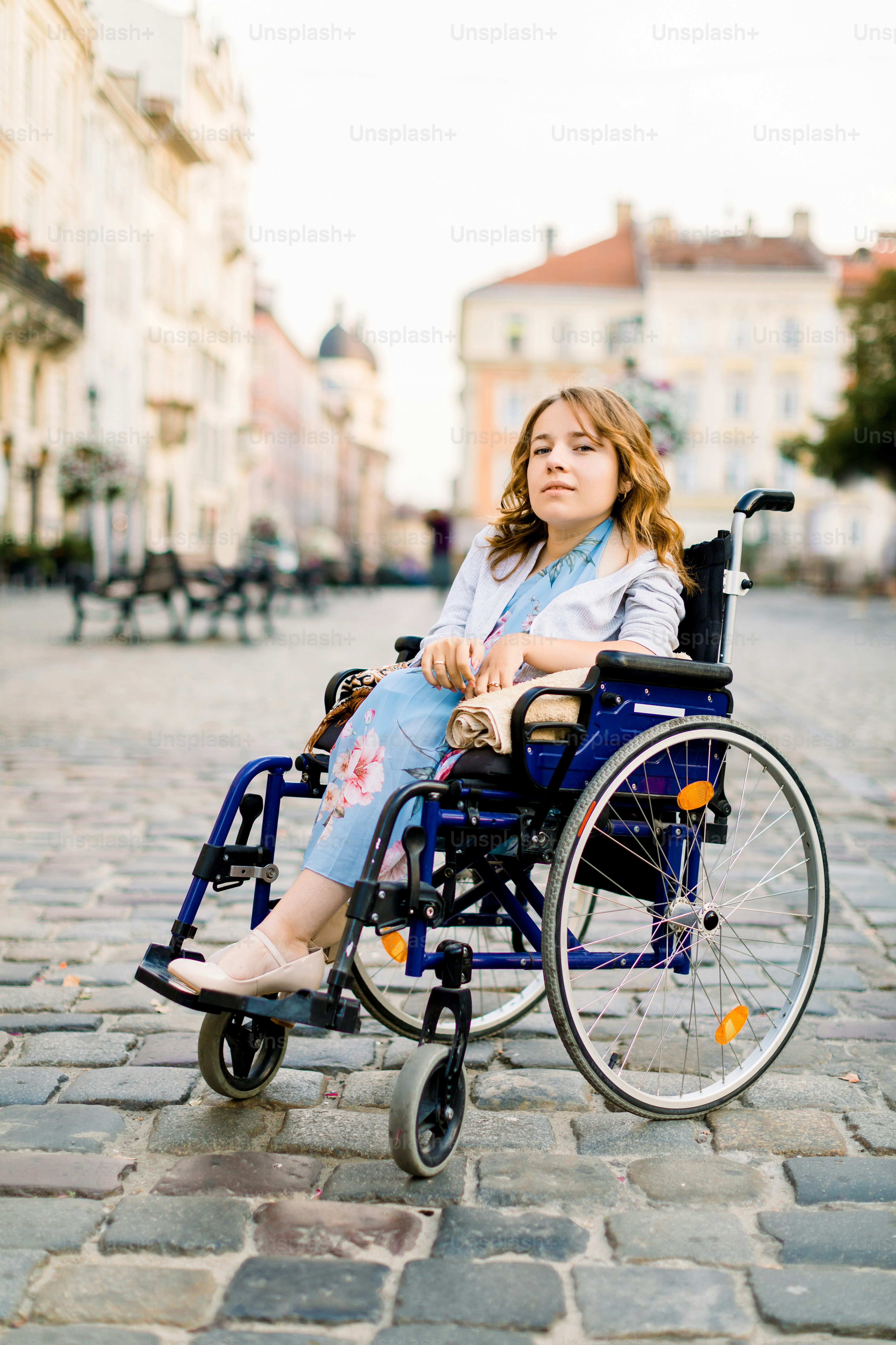 atraente mulher jovem deficiente em vestido azul sentado em uma cadeira de rodas, ao ar livre na cidade.