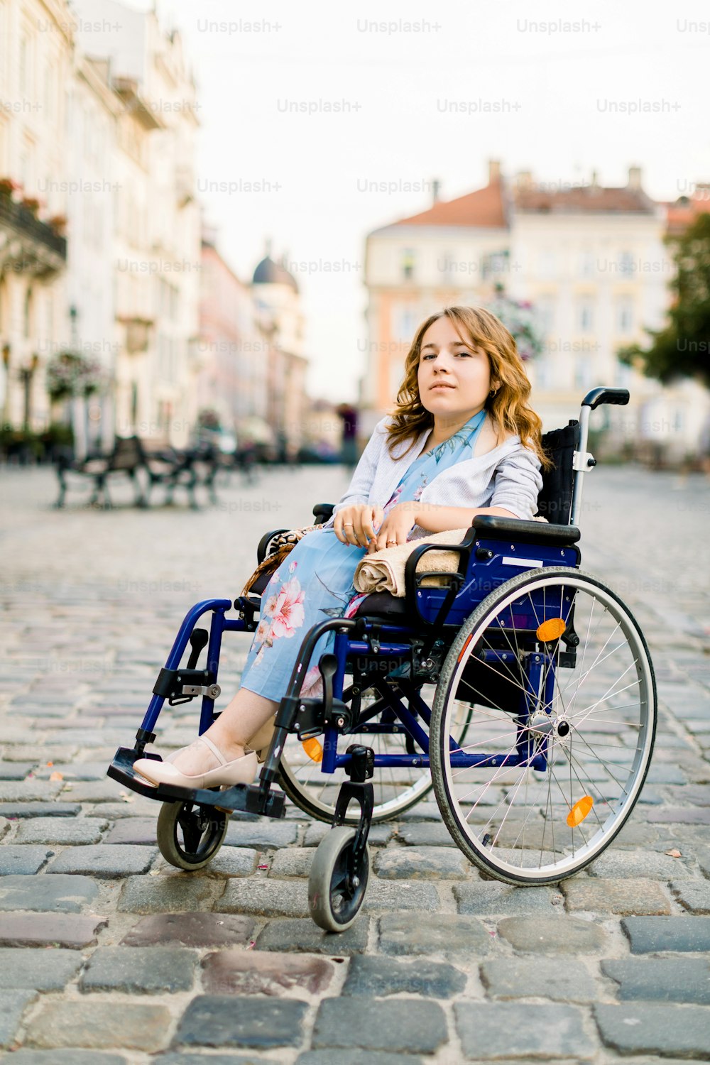 attractive disabled young woman in blue dress sitting in a wheelchair, outdoors in the city.