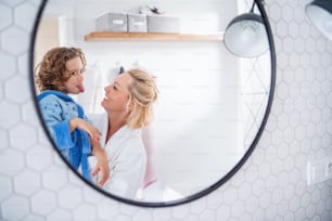 A reflection of mother and small daughter in mirror in bathroom indoors at home, making faces.