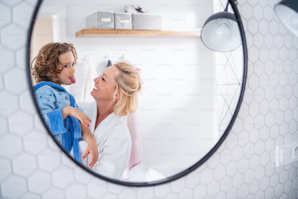 Ein Spiegelbild von Mutter und kleiner Tochter im Spiegel im Badezimmer drinnen zu Hause, Grimassen machen.