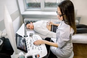 Professiona woman sonographer therapi.st working with ultrasound machine at the clinic, making kidney ultrasound for female patient, looking at the screen and pushing buttons on control panel