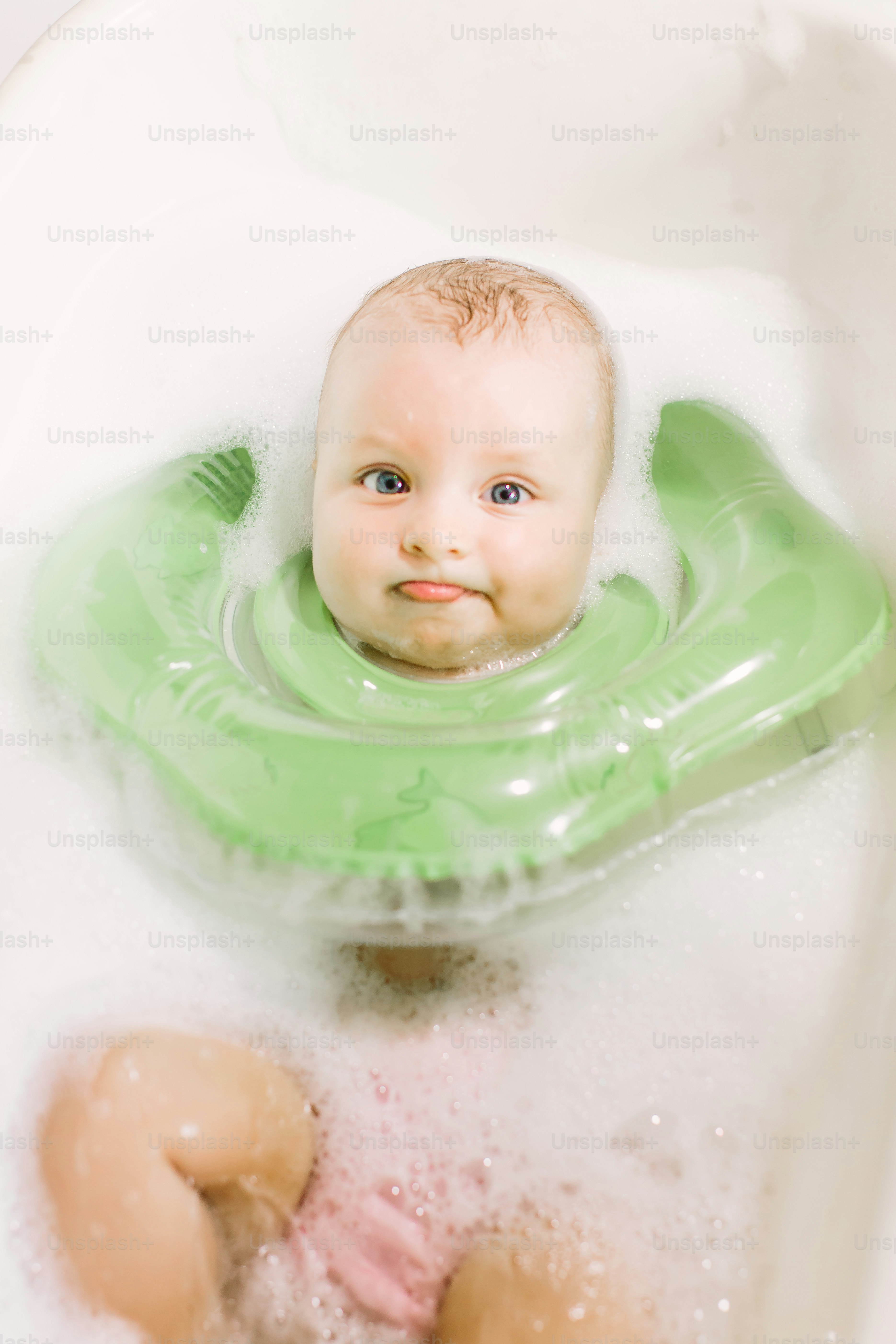 Baby swimming with green neck swim ring s in the bathtub