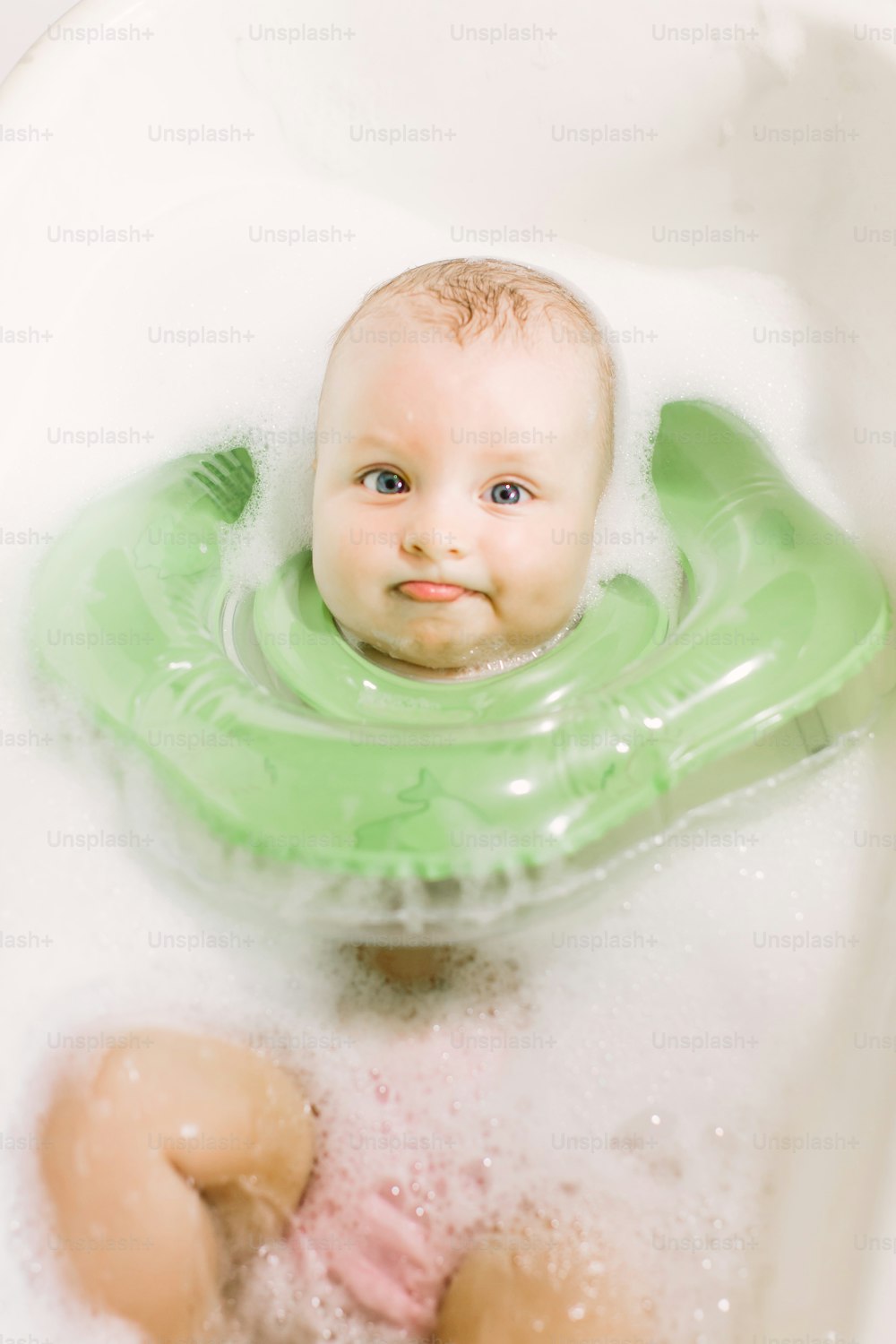 Bébé nageant avec des anneaux de bain à col vert dans la baignoire