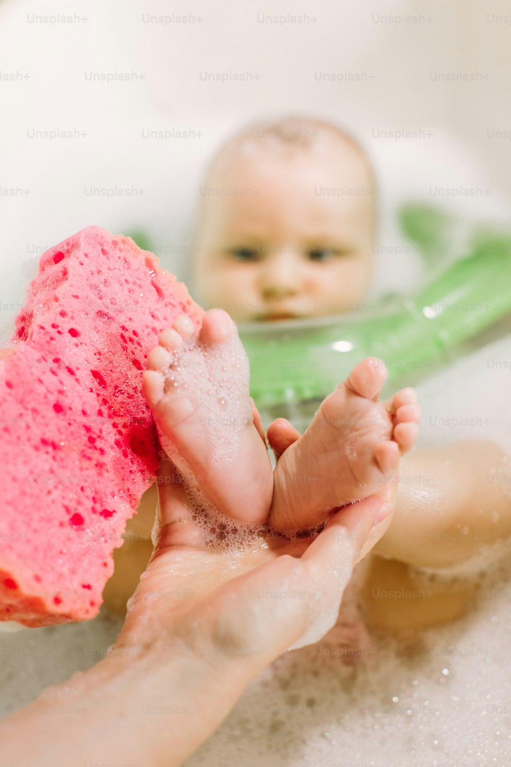 Baby swimming with green neck swim ring. mom rubs baby feet with a red sponge