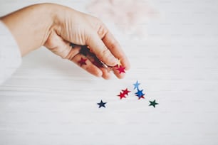 Hand holding colorful sparkling stars decorations on white background. Stylish atmospheric image. Happy birthday concept. Holiday decor. Magic in hand. Christmas