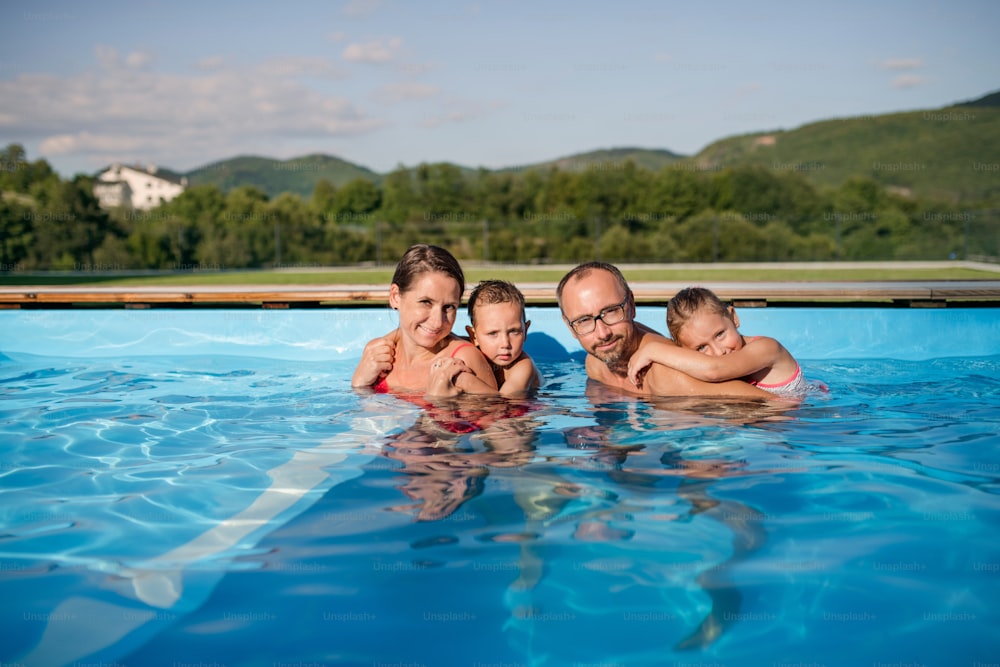 Young family with two small children in swimming pool outdoors, looking at camera.