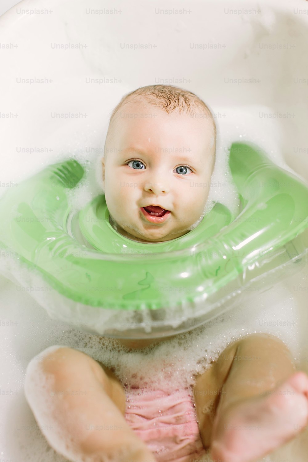 Bebé nadando con anillo de natación de cuello verde s en la bañera