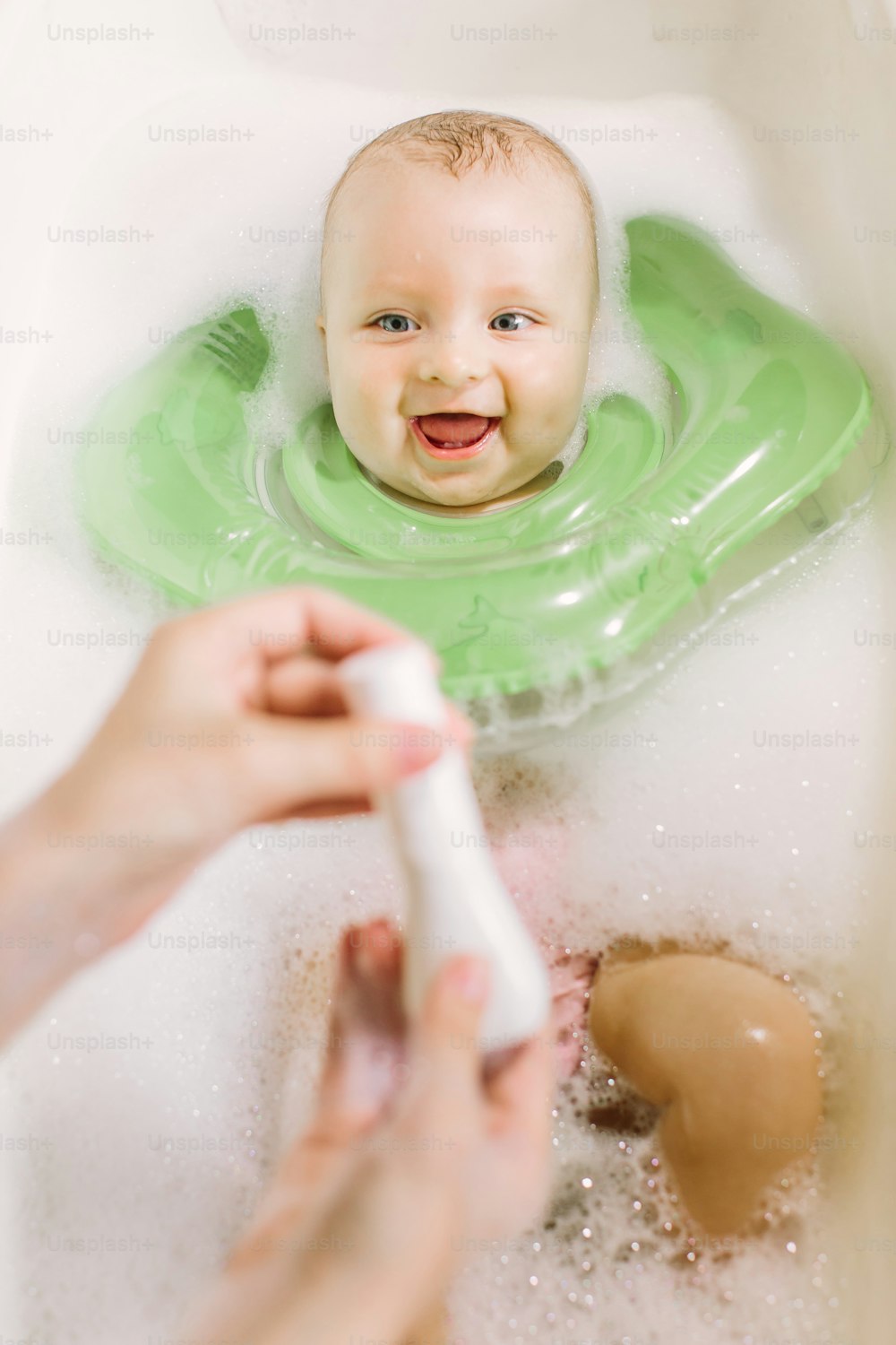 Babyschwimmen mit grünem Hals Schwimmring. Mama drückt Shampoo aus der Tube
