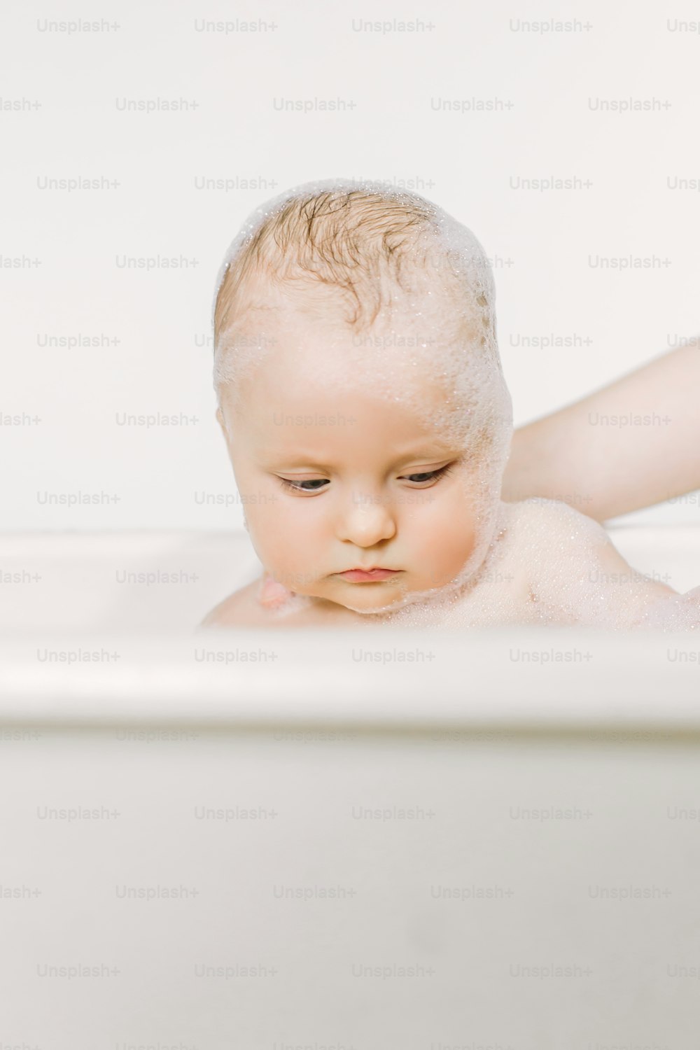 거품 거품을 가지고 노는 목욕을 하는 행복한 웃는 아기. 욕조에 있는 어린 아이. 유아 씻기 및 목욕. 어린 아이들을위한 위생 및 보살핌.