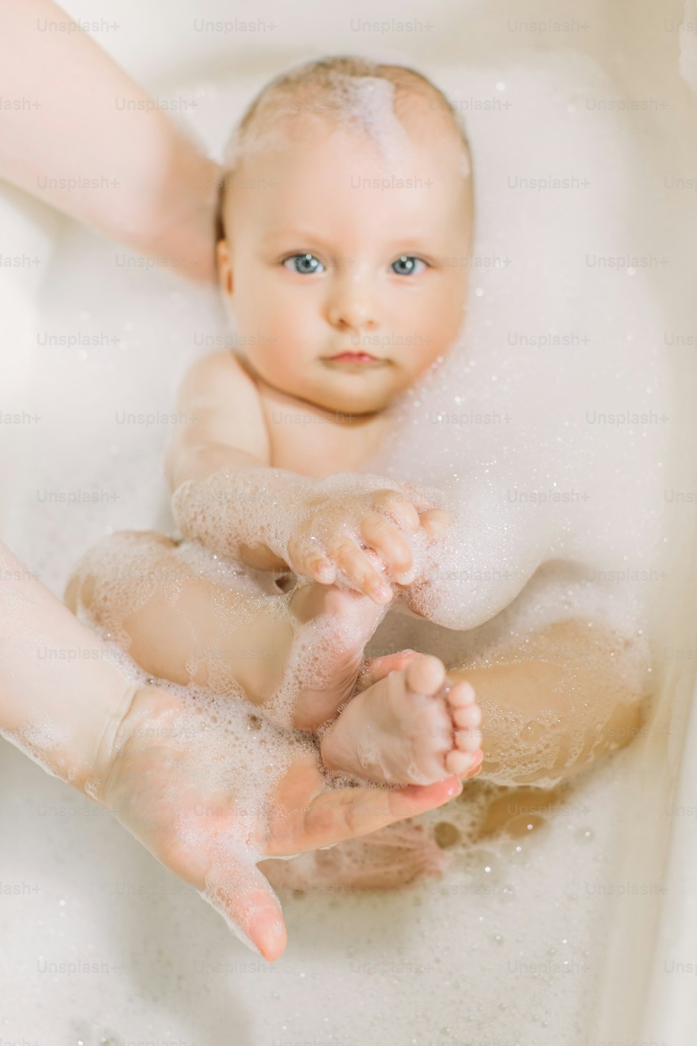 Happy laughing baby taking a bath playing with foam bubbles. Little child in a bathtub. Infant washing and bathing. Hygiene and care for young children. Newborn baby bathing