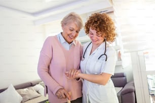 Enfermera sonriente que ayuda a la anciana a caminar por el hogar de ancianos. Retrato de una cuidadora feliz y una mujer mayor caminando juntas en casa. Cuidador profesional que cuida a una anciana.