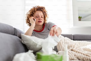 Young woman getting bad news by phone. unhappy woman talking on mobile phone looking down. Crying depressed girl holds phone sitting on sofa hopeless , breaking up, scared of threatening, mobile abuse