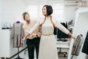 Professional designer working with his customer on a new trendy dress with female model in fashion studio. Creative people concept.