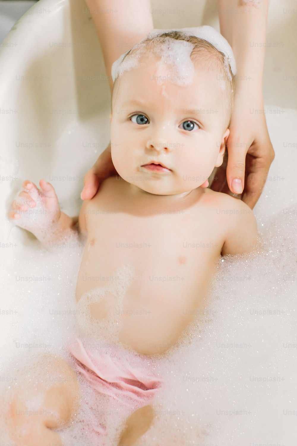 Bebé feliz riendo tomando un baño jugando con burbujas de espuma. Niño pequeño en una bañera. Niño sonriente en el baño con pato de juguete colorido. Lavado y baño de bebés. Higiene y cuidado de los niños pequeños.