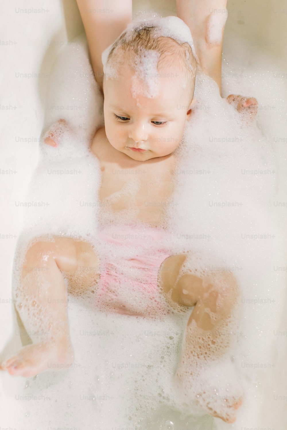 Happy laughing baby taking a bath playing with foam bubbles. Little child in a bathtub. Smiling kid in bathroom with colorful toy duck. Infant washing and bathing. Hygiene and care for young children.