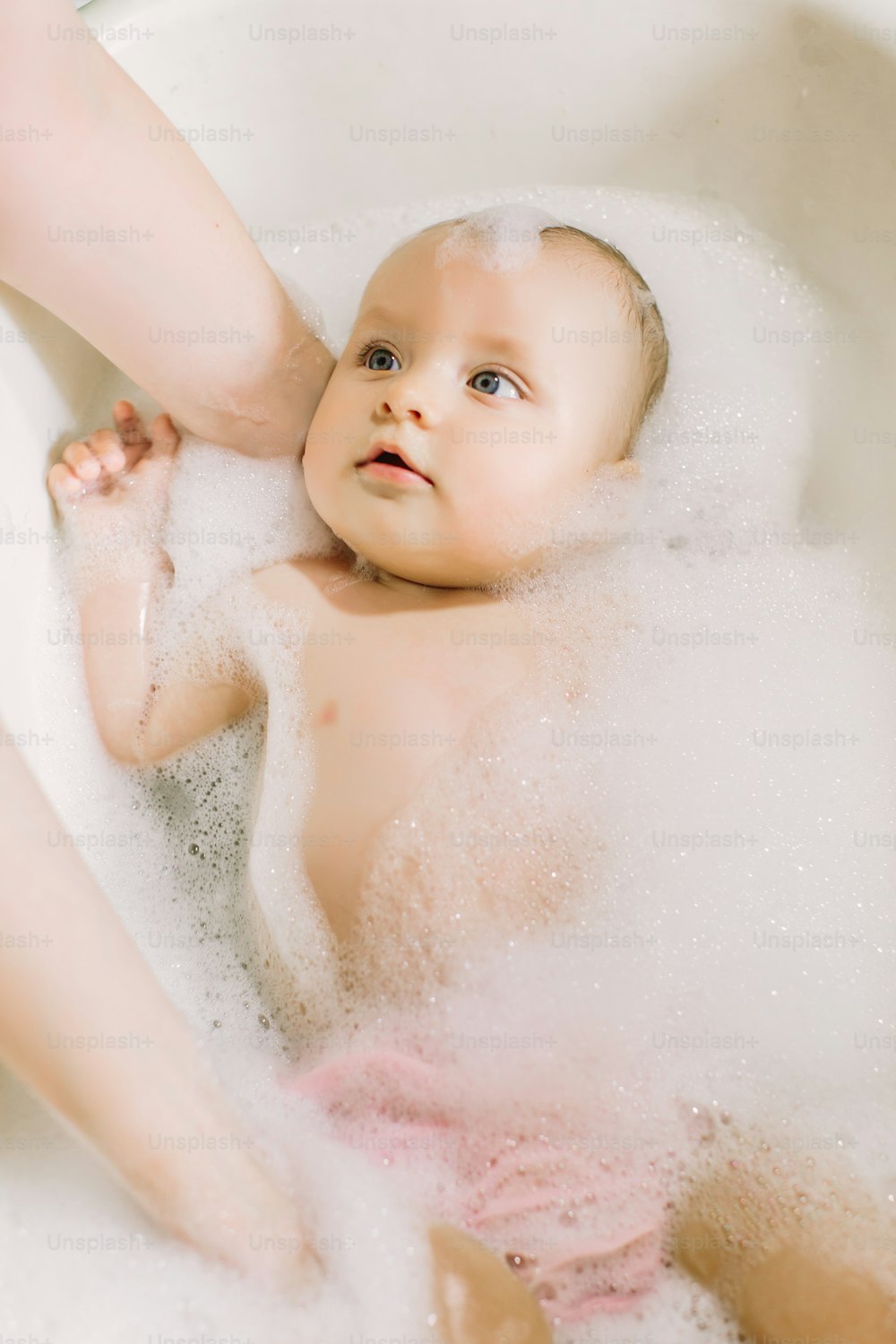 거품 거품을 가지고 노는 목욕을 하는 행복한 웃는 아기. 욕조에 있는 어린 아이. 유아 씻기 및 목욕. 어린 아이들을위한 위생 및 보살핌. 신생아 목욕